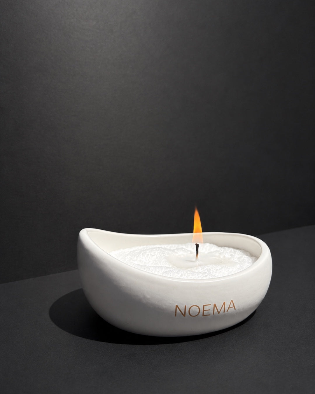 NOEMA white ceramic vessel filled with white pearled wax and a lit wick